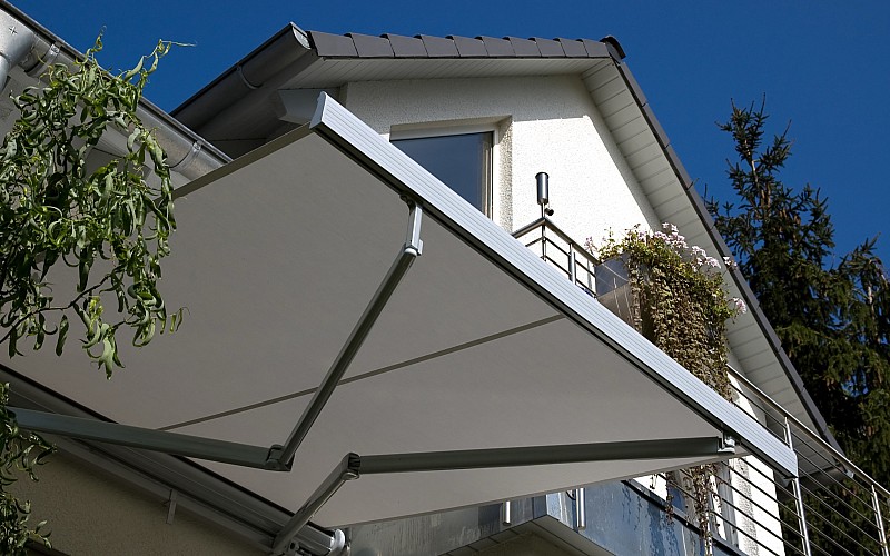 Ausgefahrene Gelenkarmmarkise an einem Balkon eines Einfamilienhauses bei sonnigem Wetter